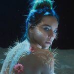 Guía completa para plantar cactus de disco en tu jardín: retrato artístico de una mujer con espinas de cactus y flores rosadas sobre la piel en un paisaje desértico iluminado.