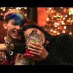 Dos jóvenes sonrientes contemplan una bola de nieve junto a un árbol iluminado; ¡Descubre qué se puede plantar en esta época para tener un jardín espectacular!