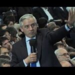 Hombre de traje hablando en una sala con micrófono y público atento, Guía completa para plantar llentias con éxito en tu jardín