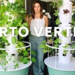 Descubre qué se puede plantar en un huerto vertical: tips y recomendaciones con dos torres de cultivo interiores llenas de hojas verdes y una mujer posando entre ellas.