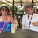 Dos personas adultas sentadas en una terraza de playa con sombreros, gafas de sol y bebidas, ¡Descubre cómo plantar tus propias uvas de playa en casa!